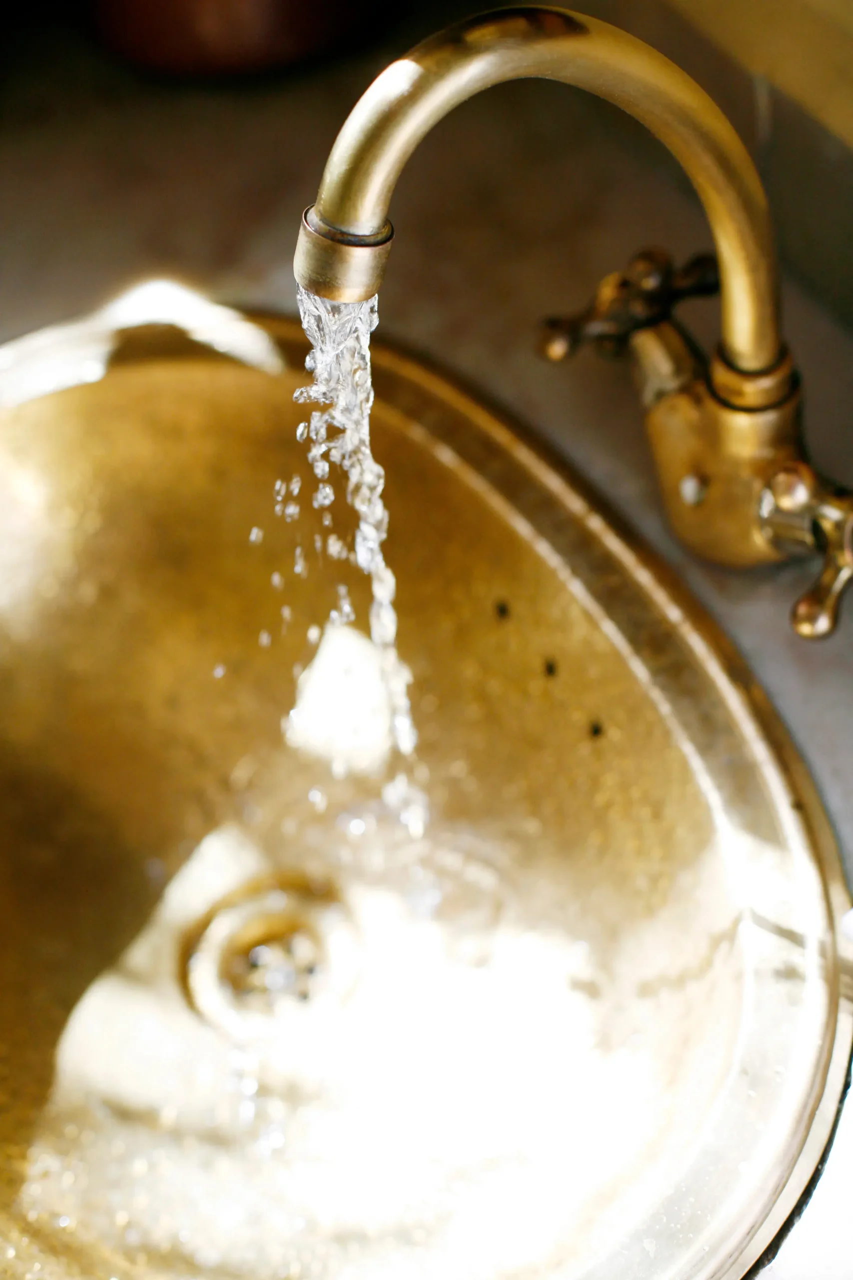 800x1080 gold hued image of water running from a faucet into a sink