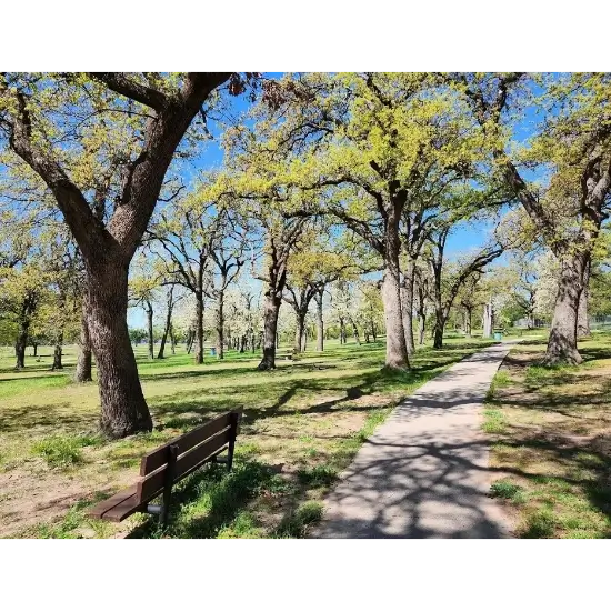 Pathway through sunny Eldon Lyon Park in Bethany, OK with green trees.