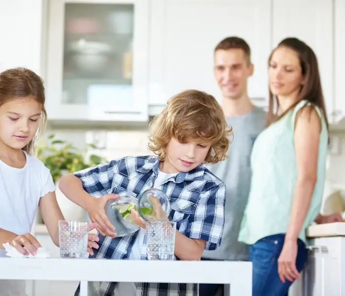 Kids preparing drinks in kitchen with parents watching.