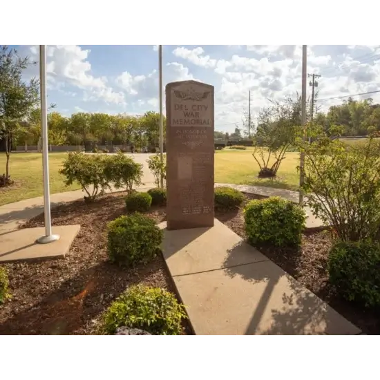 Del City War Memorial in sunny garden setting.