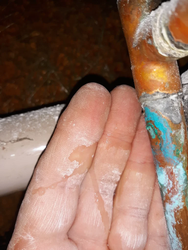 Hand touching corroded leaking copper pipe.